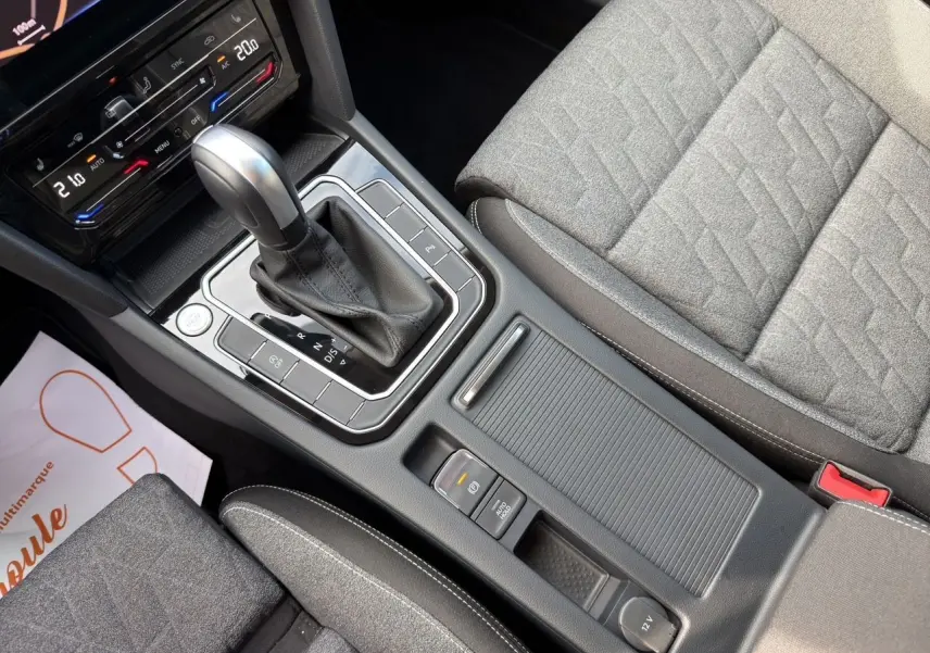 Vue rapprochée de la console centrale et levier de vitesse automatique d’une Volkswagen Passat SW 2.0 TDI, sièges tissu gris.