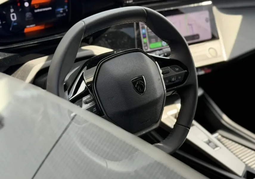 Gros plan sur le volant cuir noir et le tableau de bord numérique du Peugeot 308 SW 2025, intérieur moderne et épuré.