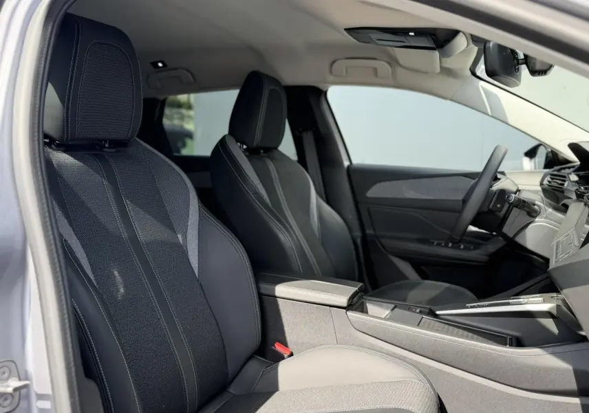Vue intérieure côté conducteur de la Peugeot 308 SW 2025, montrant les sièges en tissu et cuir noir avec surpiqûres contrastées.