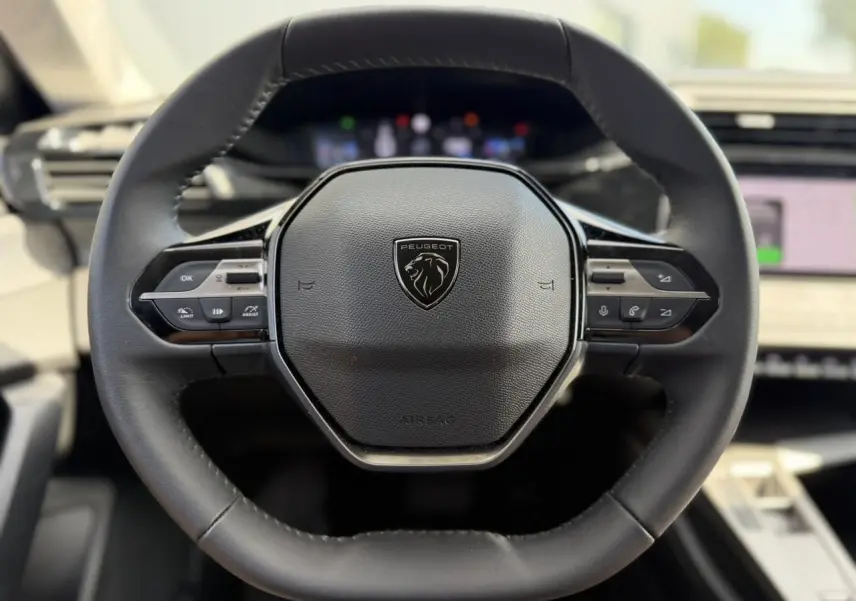 Gros plan sur le volant cuir noir du Peugeot 308 SW 2025 avec commandes intégrées et logo lion central.