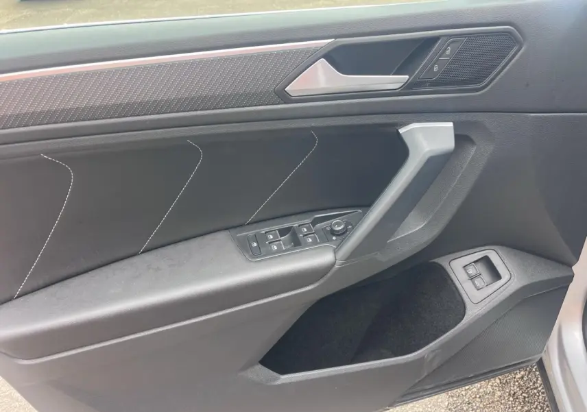 Vue intérieure côté gauche de la porte avant du Volkswagen Tiguan 2023 avec garniture noire et commandes électriques.