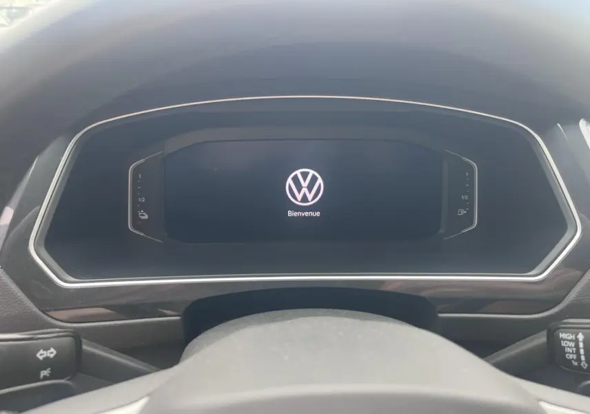 Vue rapprochée du tableau de bord numérique noir du Volkswagen Tiguan 1.4 eHybrid 2023 affichant le logo VW et "Bienvenue".