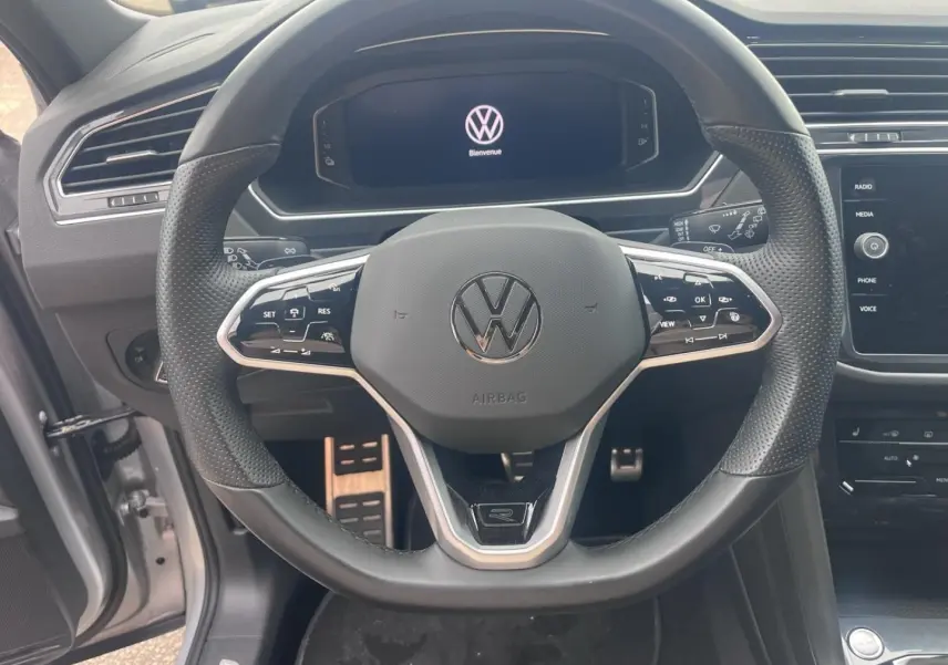 Vue rapprochée du volant cuir multifonction noir du Volkswagen Tiguan 2023 avec écran digital en arrière-plan.
