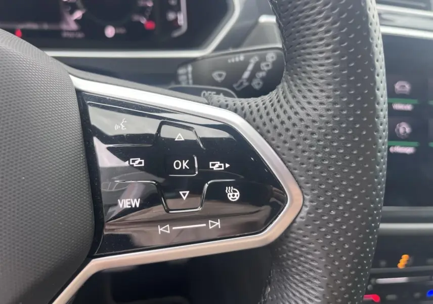 Gros plan sur les commandes multifonctions noires à gauche du volant cuir perforé du Volkswagen Tiguan gris Dauphin.