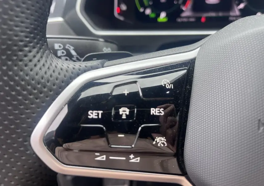 Gros plan sur les commandes de régulateur adaptatif du volant cuir perforé du Volkswagen Tiguan gris Dauphin 2023.