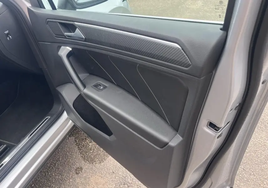 Vue intérieure de la porte avant gauche du Volkswagen Tiguan gris dauphin avec insert carbone et surpiqûres blanches.