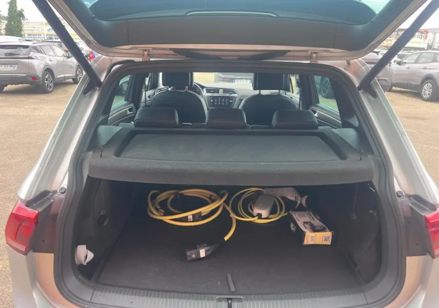 Coffre ouvert d’un Volkswagen Tiguan gris dauphin 2023, vue arrière montrant câbles de recharge hybride et intérieur noir.
