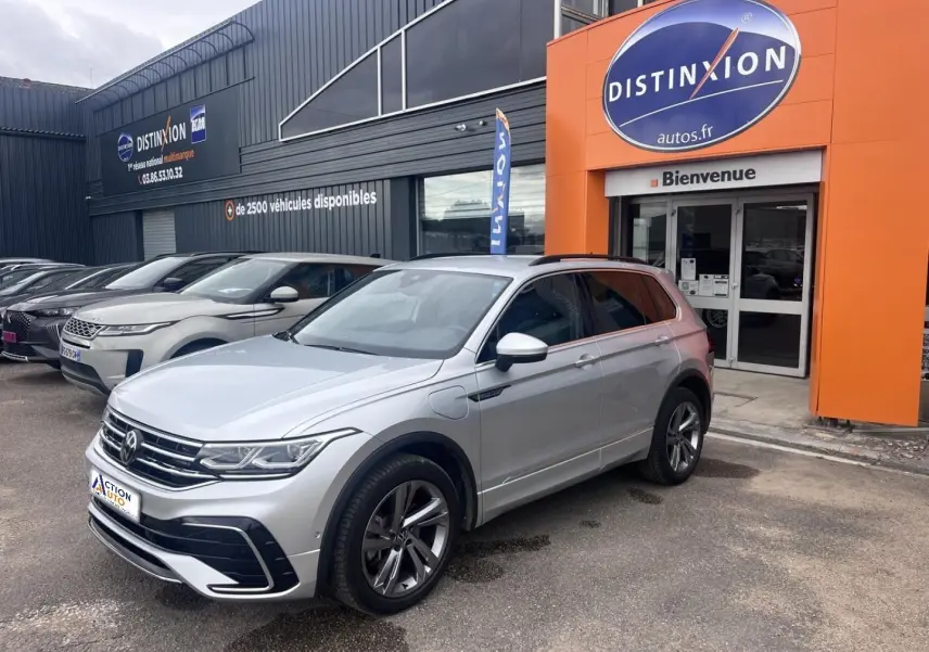 Vue 3/4 avant droit du Volkswagen Tiguan gris dauphin métallisé avec jantes alliage et toit noir devant un concessionnaire.