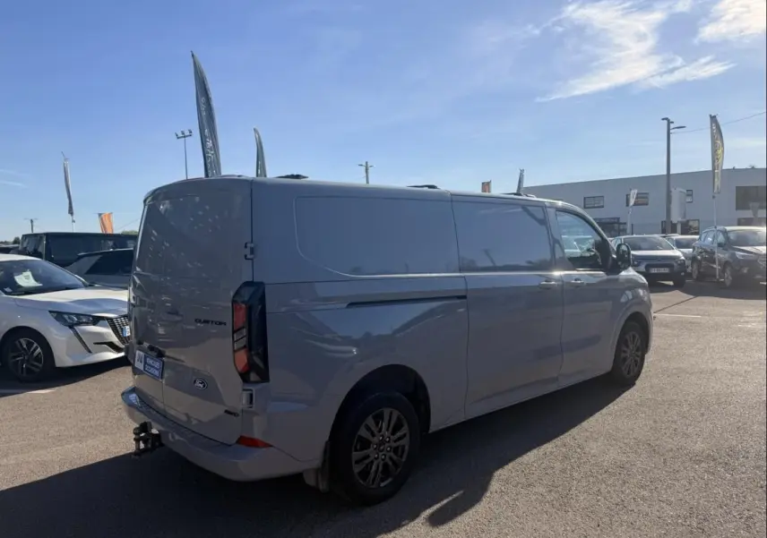 Vue 3/4 arrière droite du Ford Transit Custom Fourgon gris 2024 avec attelage et jantes foncées.