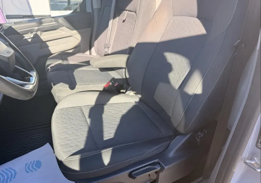 Vue intérieure côté conducteur du Ford Transit Custom Fourgon gris 2024, mettant en valeur les sièges en tissu et l'accoudoir central.
