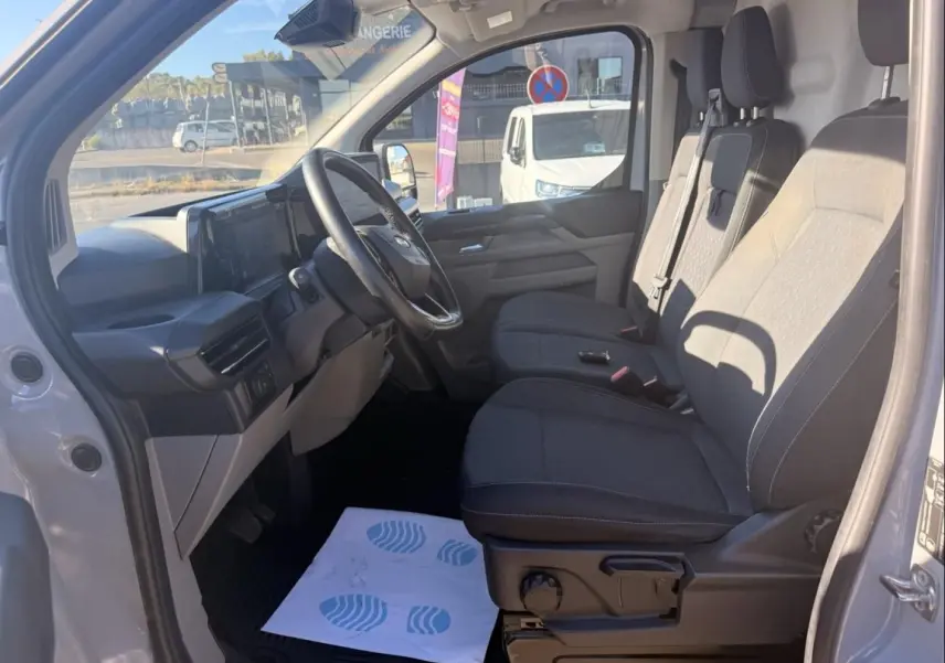 Vue intérieure côté conducteur du Ford Transit Custom Fourgon gris 2024, sièges tissu et tableau de bord moderne.