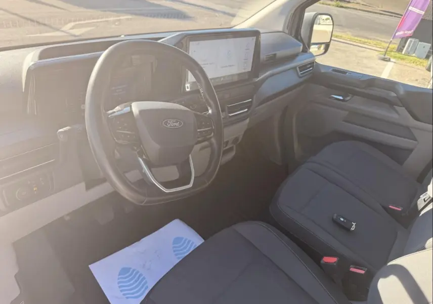 Vue intérieure côté conducteur du Ford Transit Custom Fourgon gris 2024, avec volant multifonction et écran tactile central.