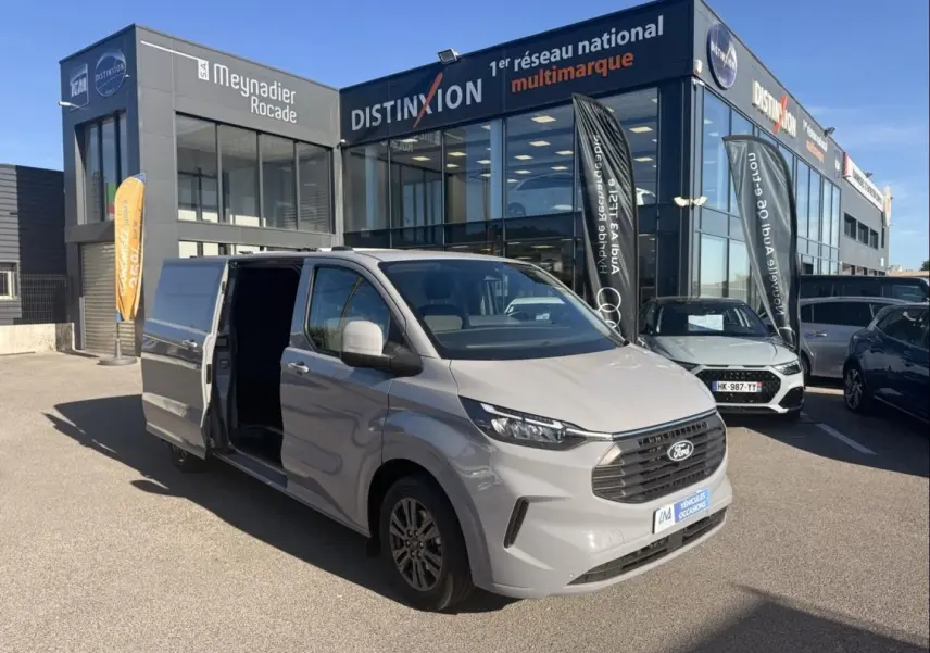 Ford Transit Custom Fourgon gris en 3/4 avant droit, porte latérale coulissante ouverte, devant un bâtiment commercial.
