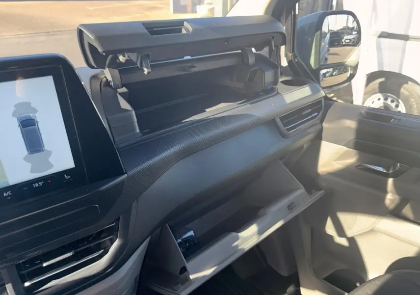 Intérieur du Ford Transit Custom 2024, vue côté passager montrant tableau de bord gris et rangements ouverts.