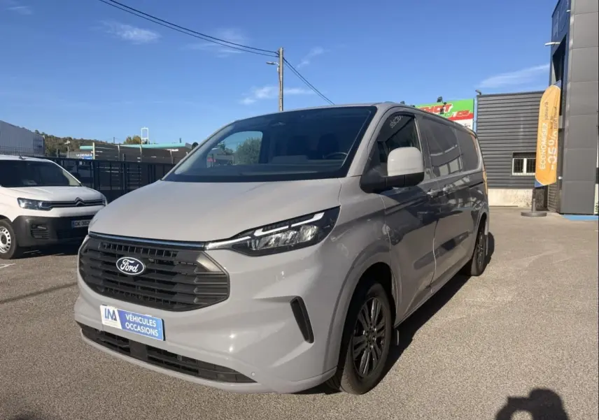 Ford Transit Custom Fourgon gris en 3/4 avant droit, avec calandre noire et jantes alliage sombres, stationné en extérieur.
