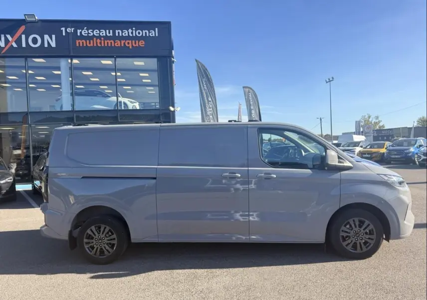 Vue de profil côté droit du Ford Transit Custom Fourgon gris 2024, finition Limited 4x4, stationné en extérieur.
