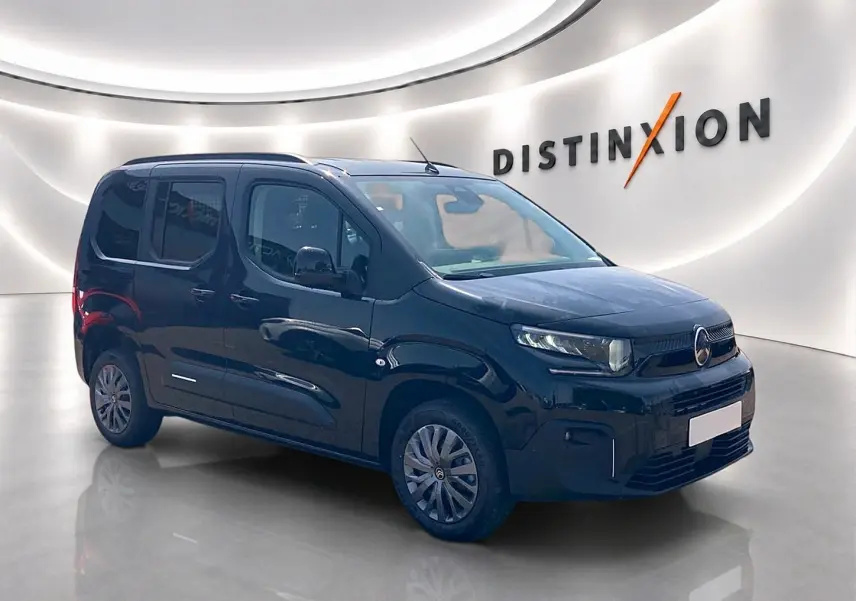 Vue 3/4 avant d’un Citroën Berlingo noir 2026 avec barres de toit et jantes alu dans un showroom lumineux.