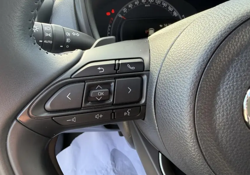 Gros plan sur les commandes au volant noir de la Toyota Aygo X 2025, avec tableau de bord partiellement visible.
