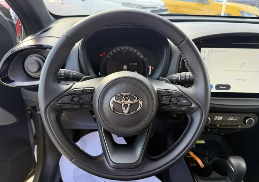 Vue intérieure centrée sur le volant noir de la Toyota Aygo X 2025 avec tableau de bord et écran tactile visibles.