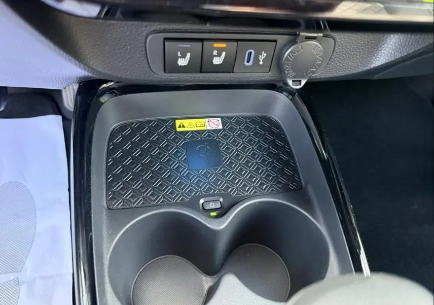 Gros plan sur la console centrale de la Toyota Aygo X 2025, montrant le chargeur sans fil, porte-gobelets et commandes de sièges chauffants.