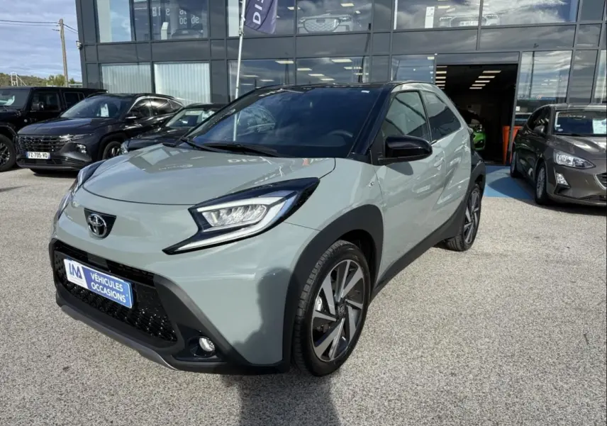 Toyota Aygo X 2025 vue 3/4 avant en vert aventurine avec toit noir, garée devant un showroom.