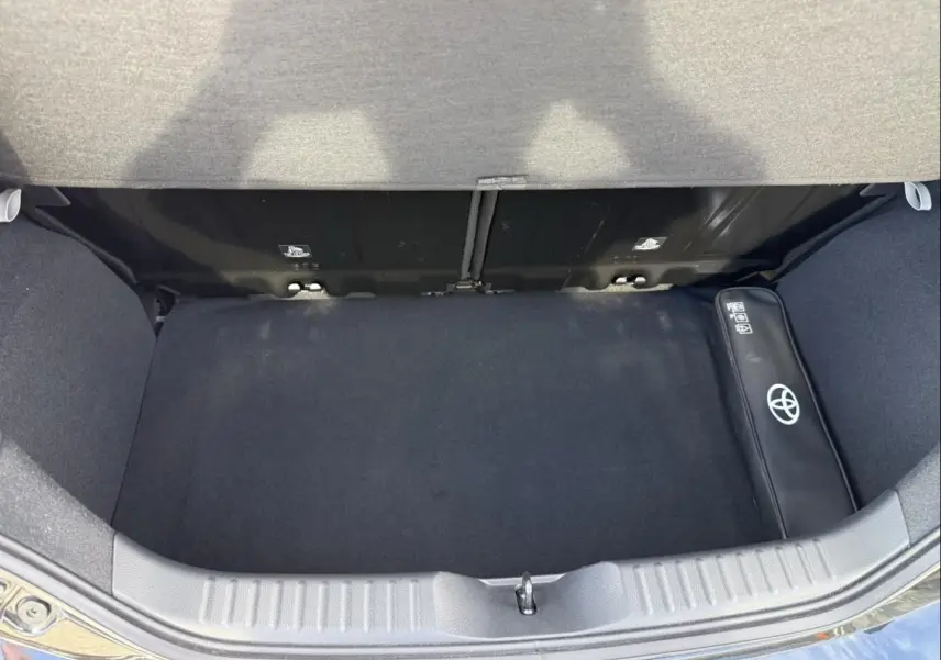 Coffre ouvert vu de dessus d’une Toyota Aygo X 2025 vert aventurine avec toit noir, sac Toyota visible à droite.