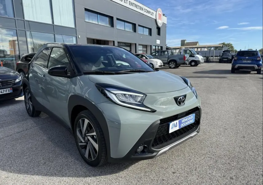 Toyota Aygo X vert aventurine avec toit noir, vue 3/4 avant droit, mettant en valeur ses phares anguleux et sa calandre noire.