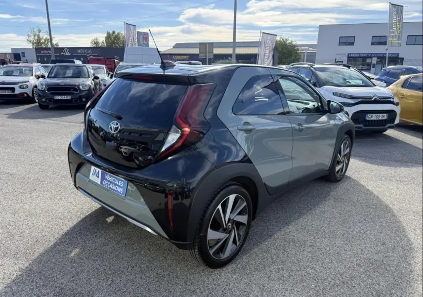 Toyota Aygo X 2025 en vert aventurine avec toit noir, vue 3/4 arrière droit, stationnée en extérieur sur parking.