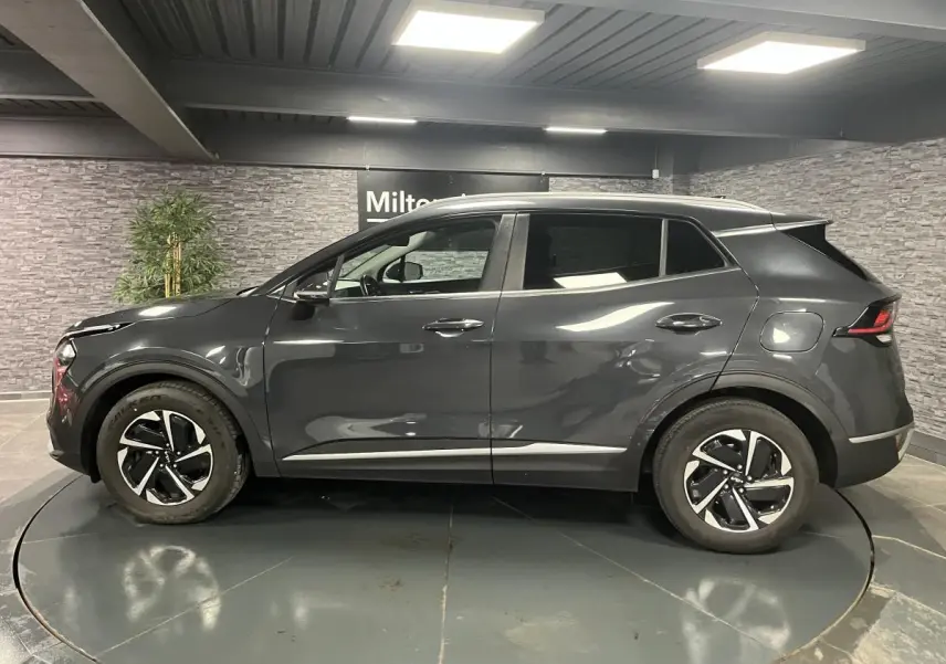 Vue latérale droite du KIA SPORTAGE gris métallisé 2022 avec jantes alliage 17 pouces et poignées chromées.