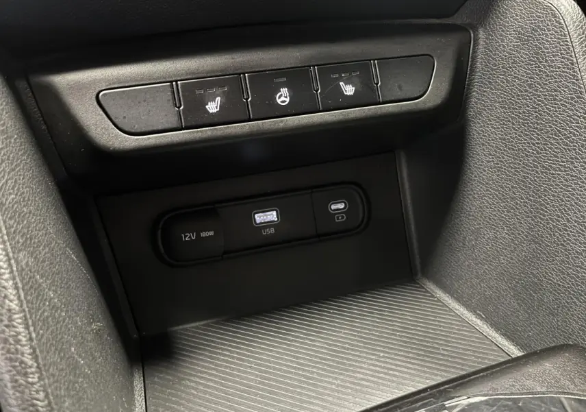Gros plan sur la console centrale du Kia Sportage gris 2022 avec ports USB, prise 12V et commandes de sièges chauffants.