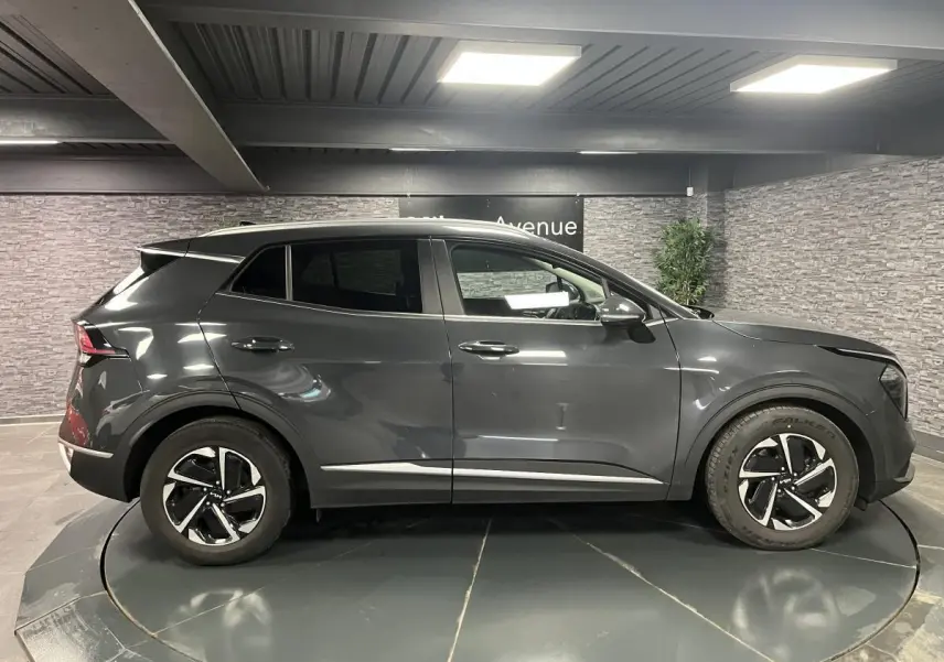 Profil côté droit du KIA SPORTAGE gris métallisé 2022 avec jantes alliage et lignes épurées en intérieur showroom.