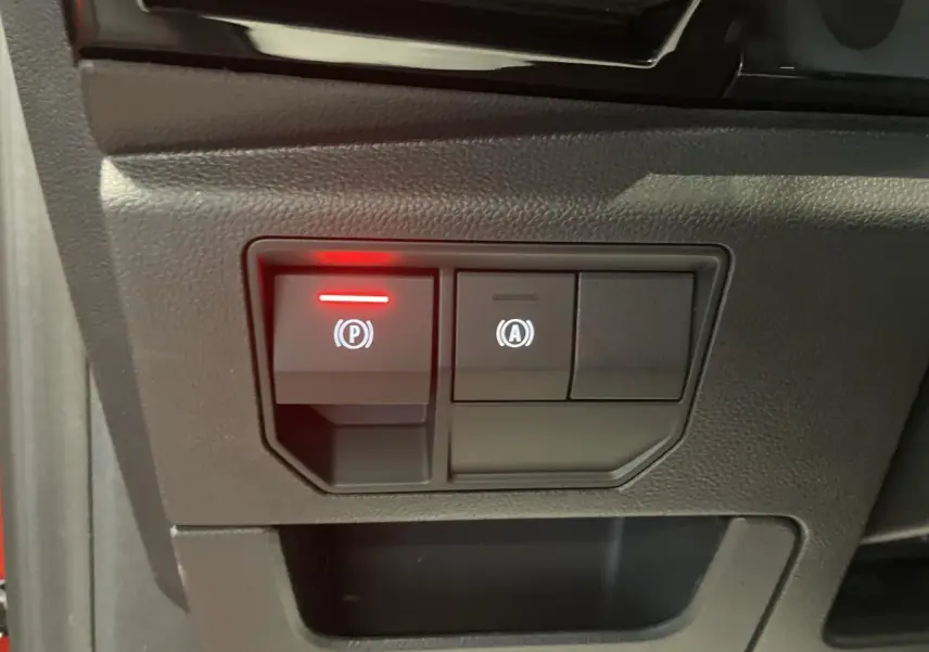 Gros plan sur les commandes du frein de parking électrique et du système start-stop du Renault Austral rouge métallisé.