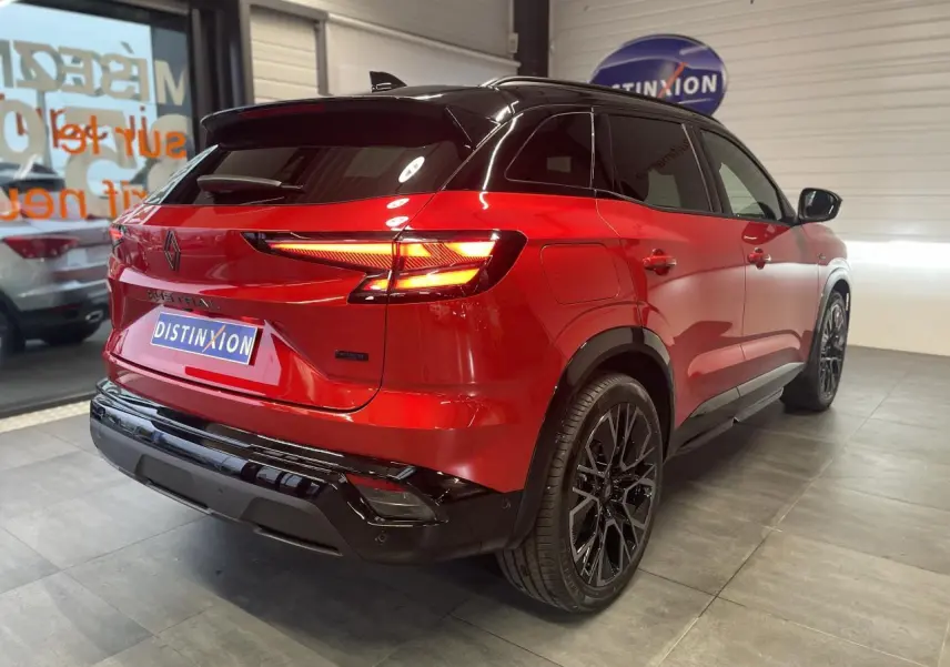 Vue 3/4 arrière droite du Renault Austral rouge métallisé avec toit noir et jantes alliage noires en showroom.