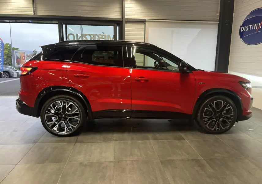 Profil droit du Renault Austral rouge métallisé avec toit noir et jantes alliage noires en showroom.