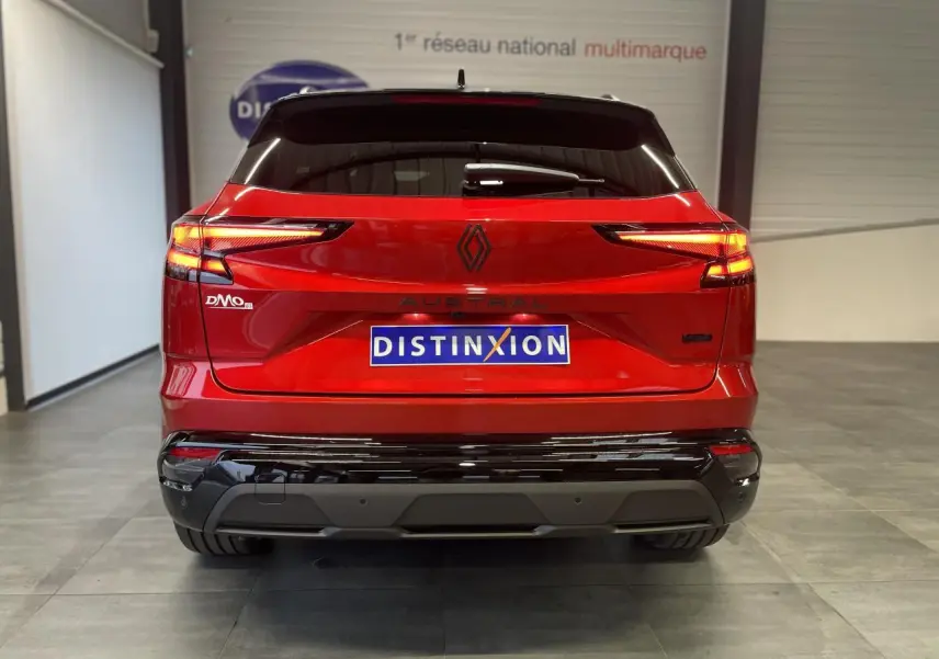 Vue arrière d'un Renault Austral rouge métallisé avec toit noir et logos noirs brillants dans un showroom.