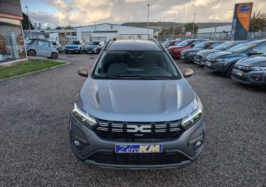 Vue avant d'un Dacia Jogger gris métallisé avec calandre noire et feux LED allumés sur un parking extérieur.