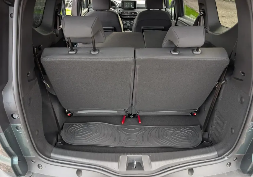 Vue arrière du coffre ouvert du Dacia Jogger gris métallisé 2025, montrant les sièges arrière rabattables et tapis de sol caoutchouc.