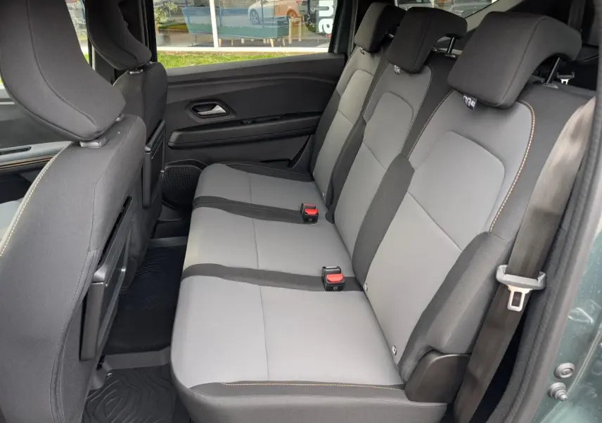 Vue latérale du siège arrière gris clair et noir du Dacia Jogger 2025 avec surpiqûres brun cuivré et tablettes aviation au dos des sièges avant.