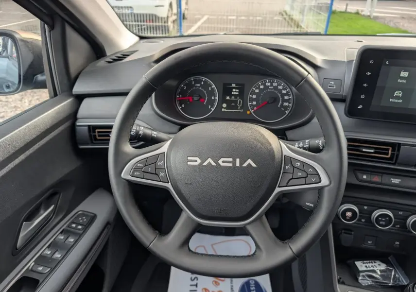 Vue intérieure centrée sur le volant noir Dacia et le tableau de bord avec écran tactile du Dacia Jogger gris métallisé 2025.
