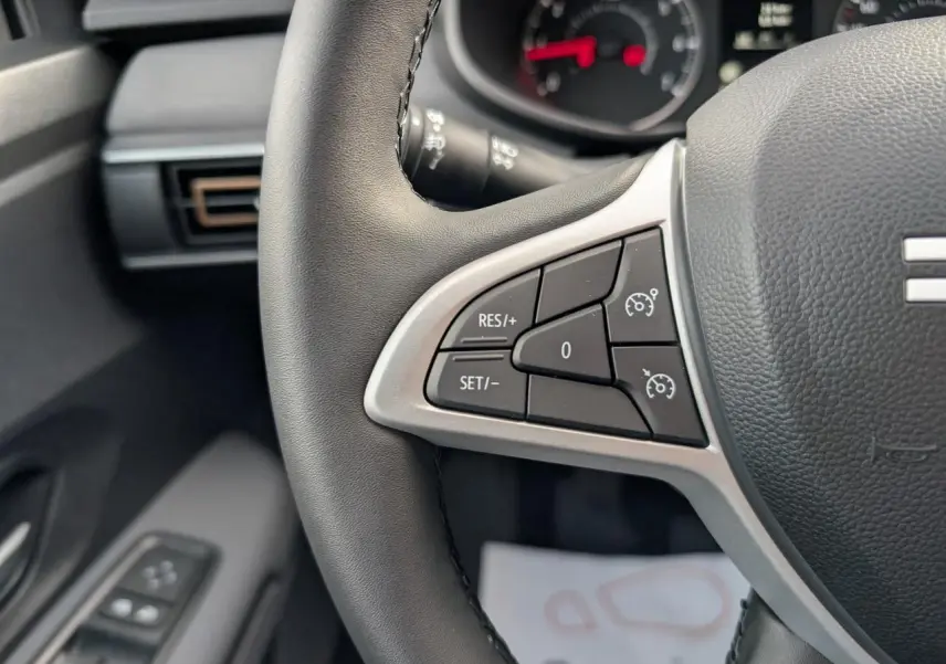 Gros plan sur les commandes du régulateur de vitesse au volant noir du Dacia Jogger 2025, intérieur gris acier.