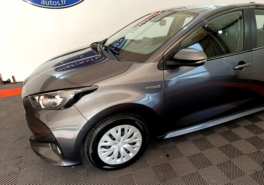 Vue 3/4 avant droit d'une Toyota Yaris hybride gris clair avec badge Hybrid visible sur l'aile avant.