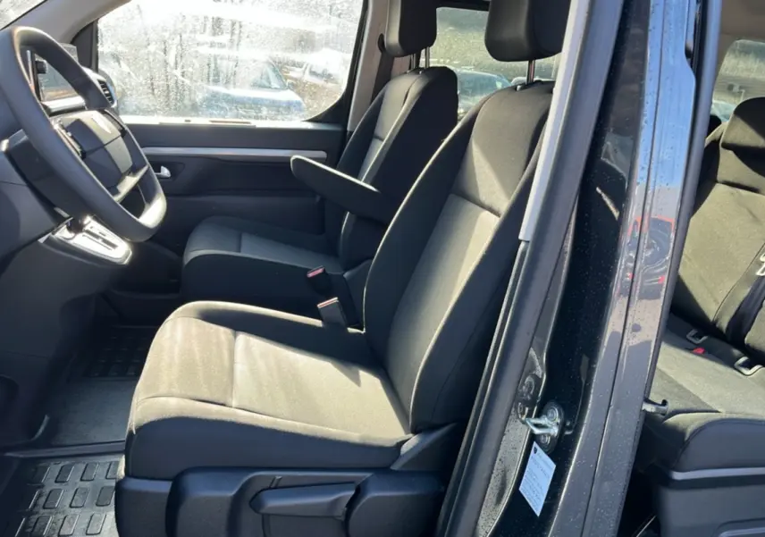 Vue intérieure côté conducteur du Peugeot Traveller gris titane 2025, sièges avant avec accoudoirs et tableau de bord visible.