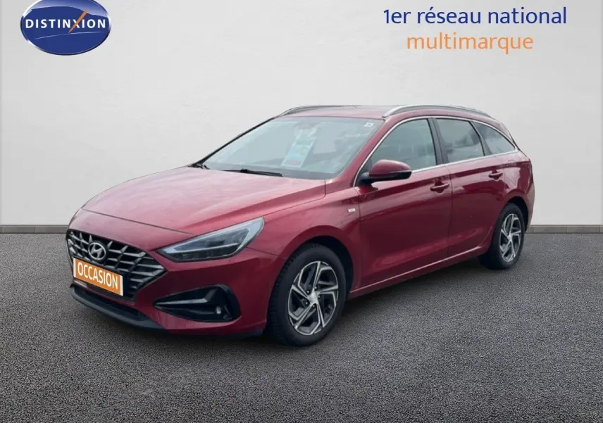 Vue 3/4 avant droite d'une Hyundai i30 SW 2023 rouge Sunset Red Metal avec jantes alliage et calandre distinctive.