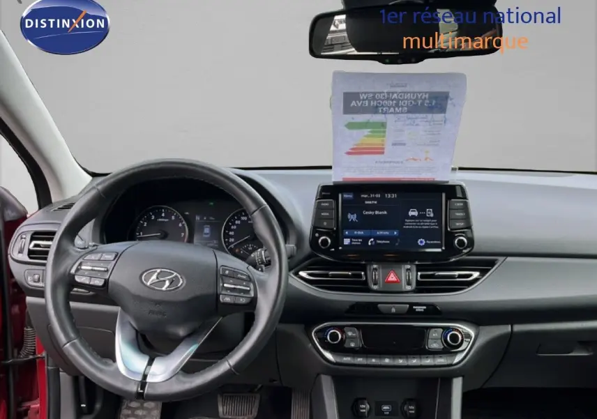 Vue intérieure frontale du tableau de bord de la Hyundai i30 SW 2023 en rouge Sunset avec écran tactile et volant cuir multifonction.