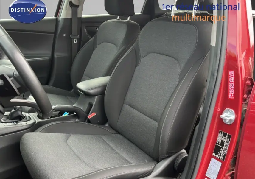 Vue intérieure côté conducteur du Hyundai i30 SW 2023, sièges tissu gris et cuir noir, portière rouge Sunset Red Metal ouverte.