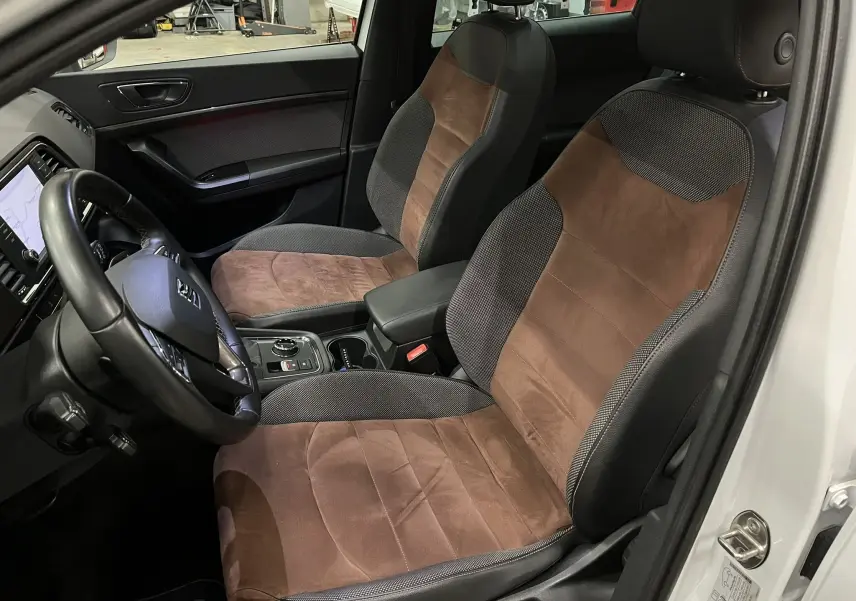 Intérieur avant du SEAT Ateca blanc, vue côté conducteur, sièges bi-matière marron et noir avec console centrale visible.