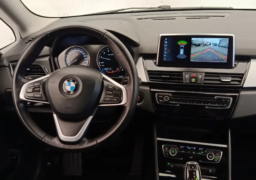 Vue intérieure centrée sur le volant cuir et alu de la BMW Série 2 Gran Tourer 218i avec écran multimédia allumé.
