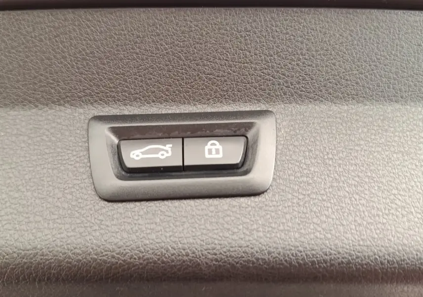 Gros plan sur les boutons d'ouverture et de verrouillage électrique du coffre d'une BMW Série 2 Gran Tourer gris clair.