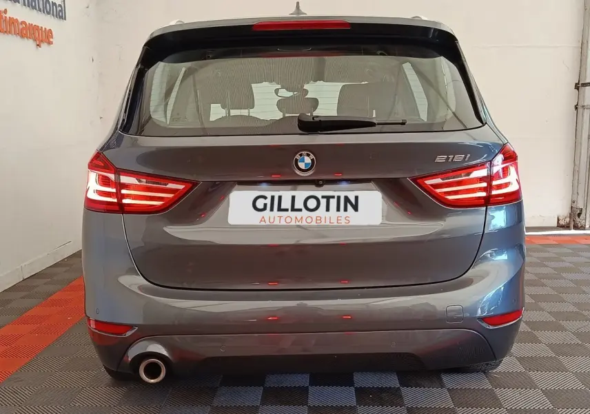 Vue arrière d'une BMW Série 2 Gran Tourer 218i Lounge gris clair avec feux LED allumés en intérieur showroom.