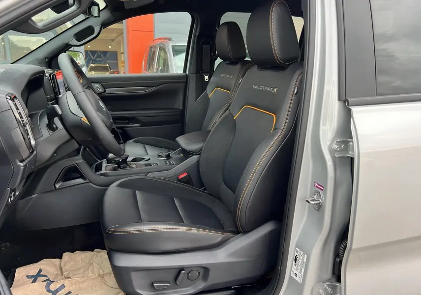Vue intérieure côté conducteur du Ford Ranger 205 Wildtrak X en gris iconic, sièges noirs avec surpiqûres orange et logo Wildtrak X brodé.